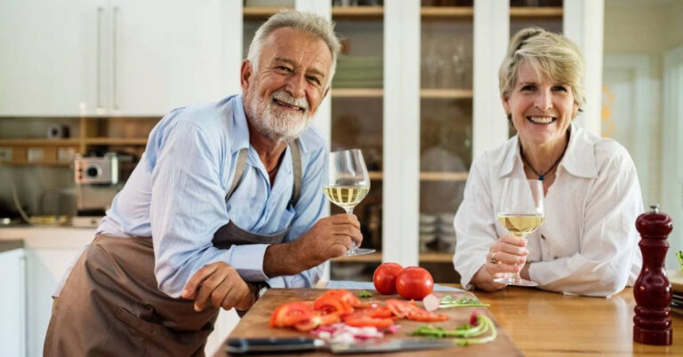 Couple âgé souriant avec du vin et des légumes dans la cuisine