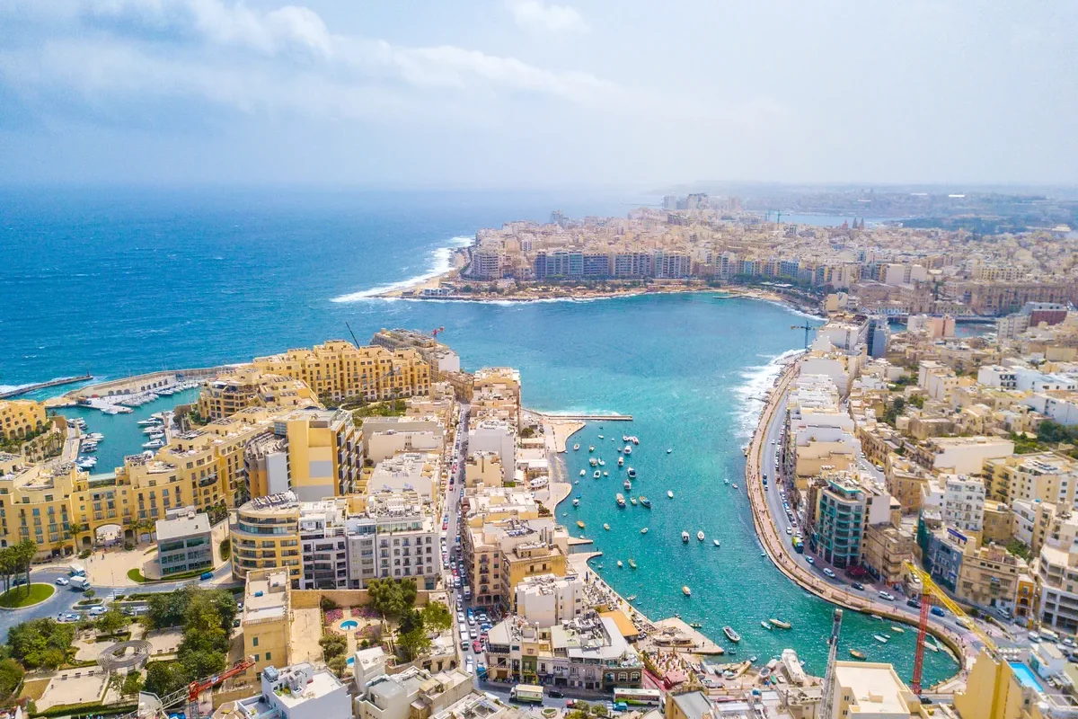 Vue aérienne de Sliema, une ville côtière de Malte, montrant ses bâtiments colorés, son port et la mer Méditerranée en arrière-plan.