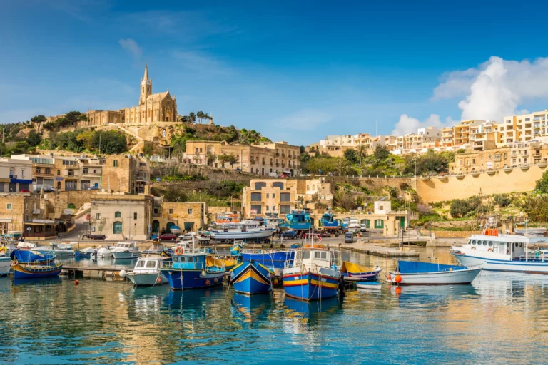 Vue pittoresque du port de Gozo, avec des bateaux colorés amarrés et la basilique surplombant la colline en arrière-plan.