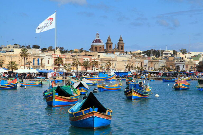 ue du port de Marsaxlokk à Malte, avec ses bateaux traditionnels colorés appelés « luzzu » et le village en arrière-plan.