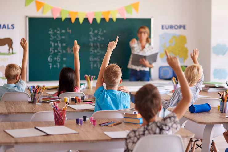 Groupe d’étudiants souriants levant la main en classe, semblant connaître la bonne réponse à une question posée.