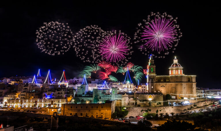 Feux d'artifice au-dessus d'une église maltaise illuminée pendant une festa traditionnelle.